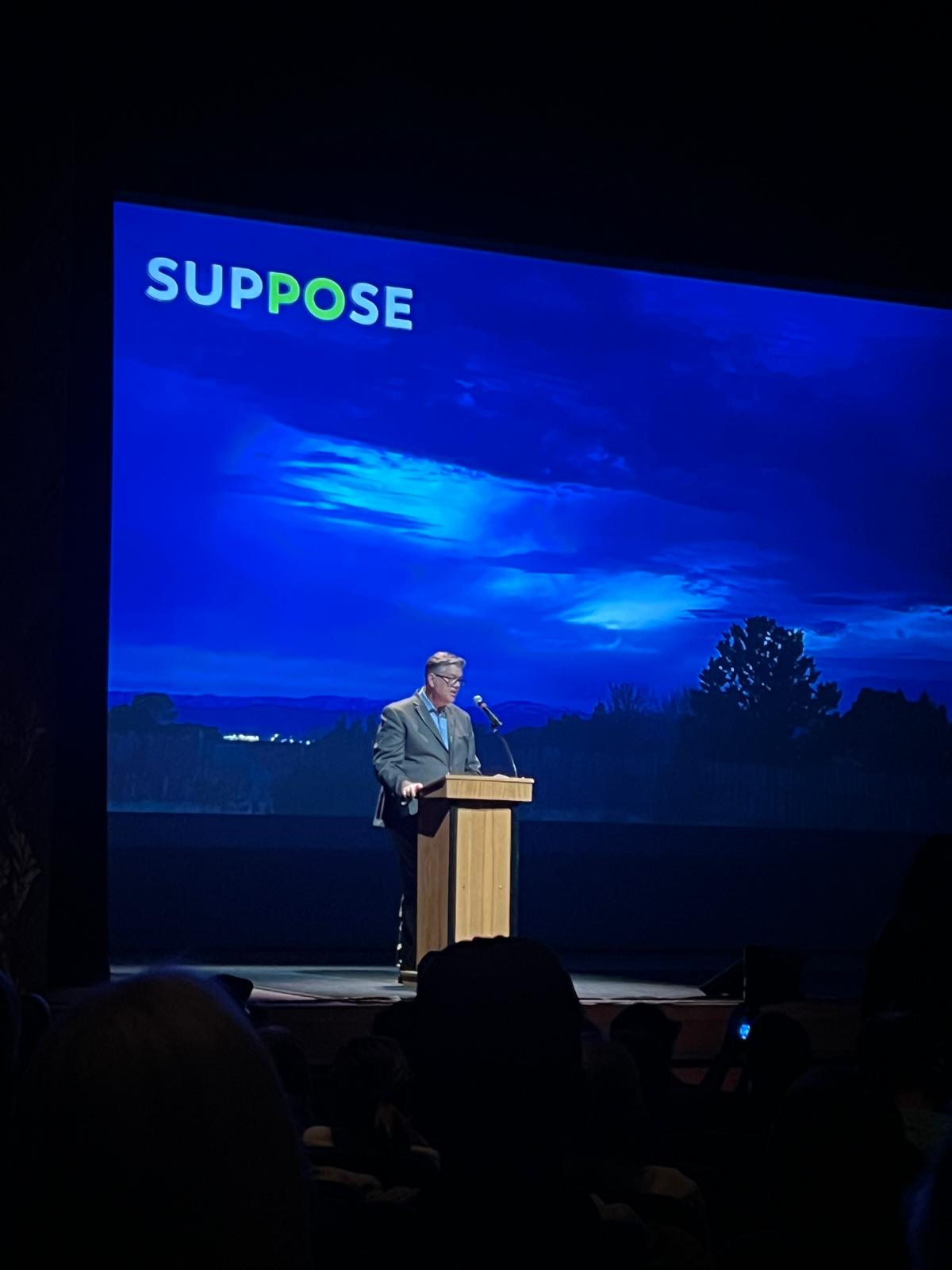 Speaking at a podium during a "Suppose" themed talk